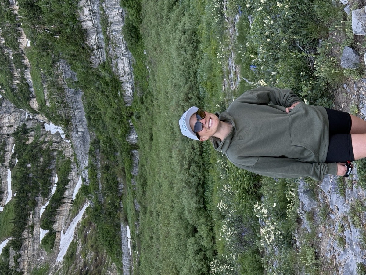 Jen smiling on a mountain trail among wildflowers